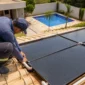 Técnico ajustando coletores de aquecimento solar de piscina em telhado com piscina residencial ao fundo