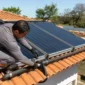 Técnico ajustando coletores de aquecimento solar de piscina em telhado com piscina residencial ao fundo