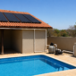 Piscina residencial com coletores solares pretos no telhado e tubulação ligada à casa de máquinas