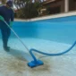 Técnico aspirando sedimentos no fundo da piscina com mangueira e cabo telescópico