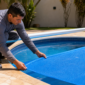 Técnico instalando capa térmica azul tipo bolha em piscina residencial com enrolador metálico