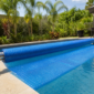 Capa térmica azul de bolhas sendo desenrolada sobre piscina residencial com enrolador metálico