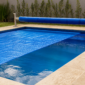 Capa térmica azul parcialmente estendida sobre piscina residencial com rolo enrolador na borda