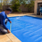 Técnico medindo a borda de uma piscina coberta com capa térmica azul para dimensionamento correto
