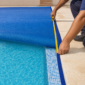 Técnico medindo capa térmica azul instalada sobre piscina residencial com fita métrica na borda