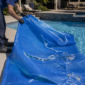 Técnico inspecionando capa térmica azul rasgada na piscina