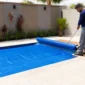 Técnico desenrolando capa térmica azul sobre piscina residencial para reduzir perda de calor e evaporação