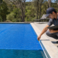 Técnico medindo borda de piscina residencial coberta parcialmente com capa térmica azul