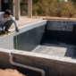 Piscina de alvenaria em construção com impermeabilização tubulações e técnico medindo nível em Goiás