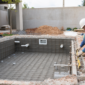 Técnico conferindo nível em piscina de alvenaria em construção com ferragem tubulação e dispositivos hidráulicos aparentes