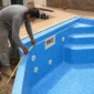 Técnico medindo borda e vinil azul em piscina residencial em construção com dispositivos hidráulicos instalados
