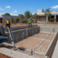 Obra de piscina residencial com estrutura de concreto, ferragens, tubulações hidráulicas e técnicos medindo o nível da borda