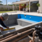 Piscina residencial em construção com técnico medindo borda e sistema hidráulico ao lado