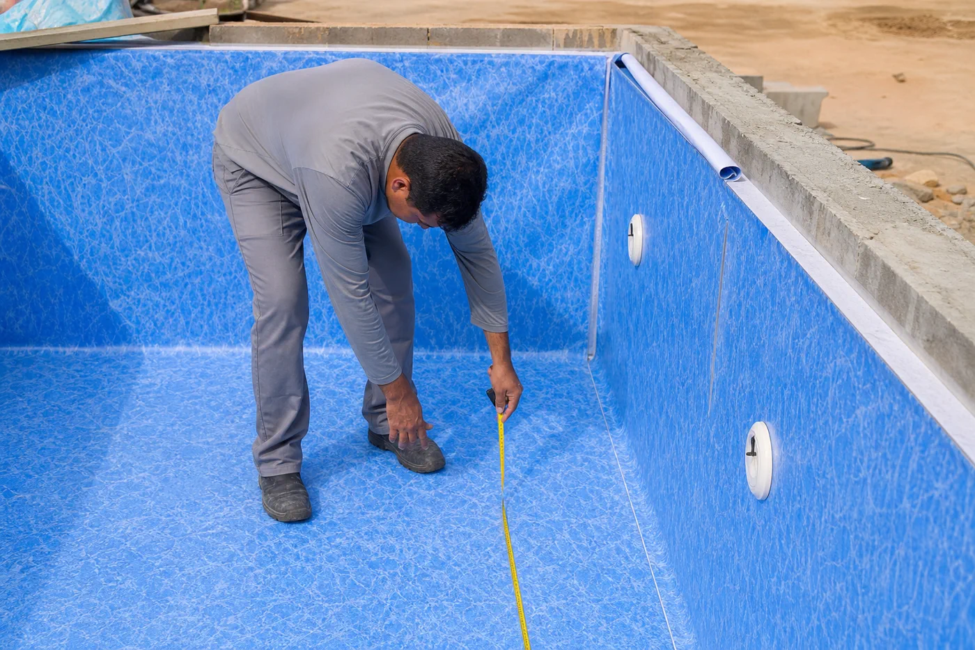 Técnico medindo vinil azul em piscina residencial em construção com dispositivos hidráulicos instalados