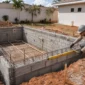 Piscina de alvenaria em construção com blocos armadura hidráulica embutida e técnico medindo o nível da borda