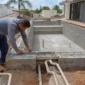 Técnico conferindo nível, estrutura de concreto e tubulação hidráulica durante construção de piscina no Setor Campinas em Goiânia