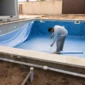 Técnico medindo vinil azul e tubulações hidráulicas em piscina residencial em obra