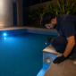 Técnico observando luminária LED de piscina com uma luz azul acesa e outra fraca durante inspeção noturna