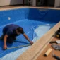 Técnico medindo piscina vazia com revestimento vinílico azul sendo instalado durante troca de vinil