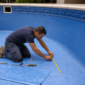 Técnico medindo vinil azul no fundo de uma piscina vazia durante troca de revestimento