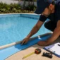 Técnico inspecionando borda e revestimento vinílico azul de piscina com trena e prancheta