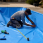 Técnico instalando vinil azul em piscina residencial vazia com trena rolo e soprador térmico no piso