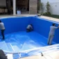 Técnicos instalando revestimento de vinil azul em piscina residencial