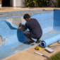 Técnico removendo revestimento vinílico antigo em piscina residencial vazia com rolo de vinil e ferramentas na borda