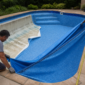 Técnicos instalando novo vinil azul em piscina residencial com manta parcialmente posicionada e bordas sendo ajustadas
