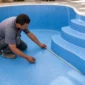 Técnico medindo novo vinil azul durante troca de revestimento em piscina residencial