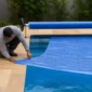 Técnico ajustando capa térmica azul com rolo enrolador em piscina residencial