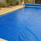 Capa térmica azul com bolhas cobrindo uma piscina residencial e rolo enrolador na borda