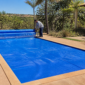 Capa térmica azul cobrindo piscina residencial com técnico conferindo enrolador e encaixe da manta
