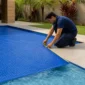 Técnico medindo capa térmica azul instalada sobre piscina residencial para ajuste correto