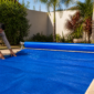 Técnico conferindo a borda de uma capa térmica azul instalada sobre piscina residencial, com enrolador metálico ao lado
