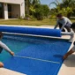 Técnicos medindo capa térmica azul com rolo enrolador em piscina residencial