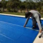 Técnico medindo capa térmica azul instalada sobre piscina residencial com enrolador lateral metálico