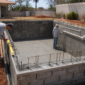 Obra de piscina de alvenaria com trabalhadores conferindo nível e tubulações