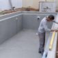 Piscina residencial em obra com técnico conferindo nível, tubulações hidráulicas e estrutura preparada para vinil