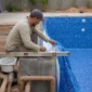 Técnico medindo piscina de vinil em construção com tubulações hidráulicas aparentes