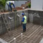 Obra de piscina de alvenaria com ferragens, tubulação hidráulica e técnicos medindo a estrutura