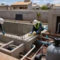 Técnicos medindo estrutura de piscina residencial em construção com ferragens, tubulações e filtro ao lado