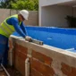 Técnico medindo nível em piscina de vinil em construção com tubulações hidráulicas aparentes