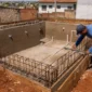 Piscina em construção com ferragem tubulações hidráulicas e técnico medindo o nível da estrutura