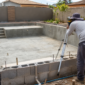 Piscina de alvenaria em construção com armadura hidráulica embutida e técnico conferindo o nível da borda