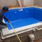 Técnico medindo piscina de vinil em construção com tubulações hidráulicas aparentes
