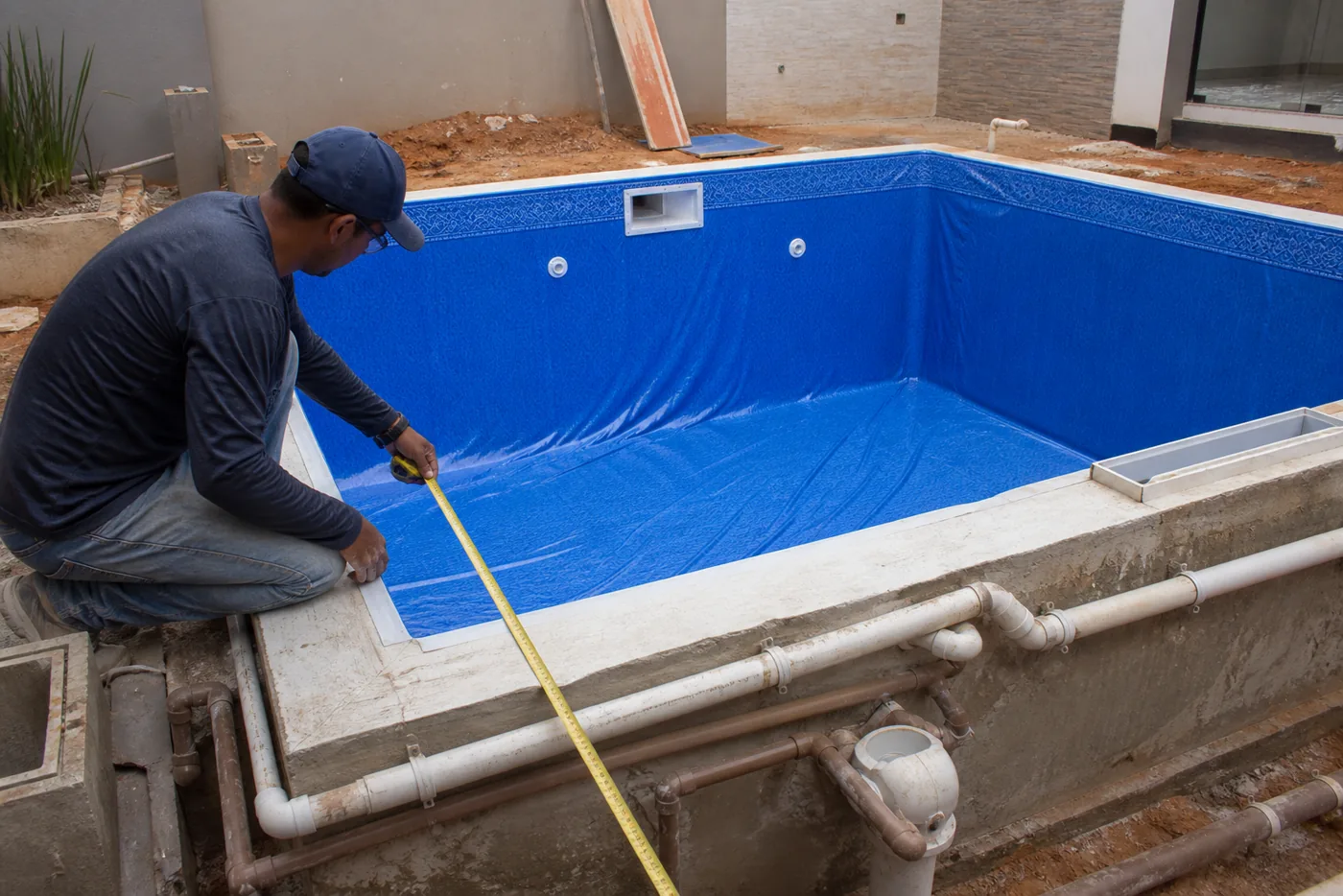 Técnico medindo piscina de vinil em construção com tubulações hidráulicas aparentes