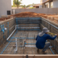 Piscina em construção com armadura, tubulações hidráulicas e técnico conferindo o nível da estrutura no Rosa dos Ventos, Aparecida de Goiânia