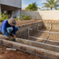 Piscina de alvenaria em construção com estrutura reforçada e técnico conferindo medidas e tubulações