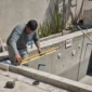 Técnico medindo estrutura de piscina em construção com nível e tubulações hidráulicas aparentes